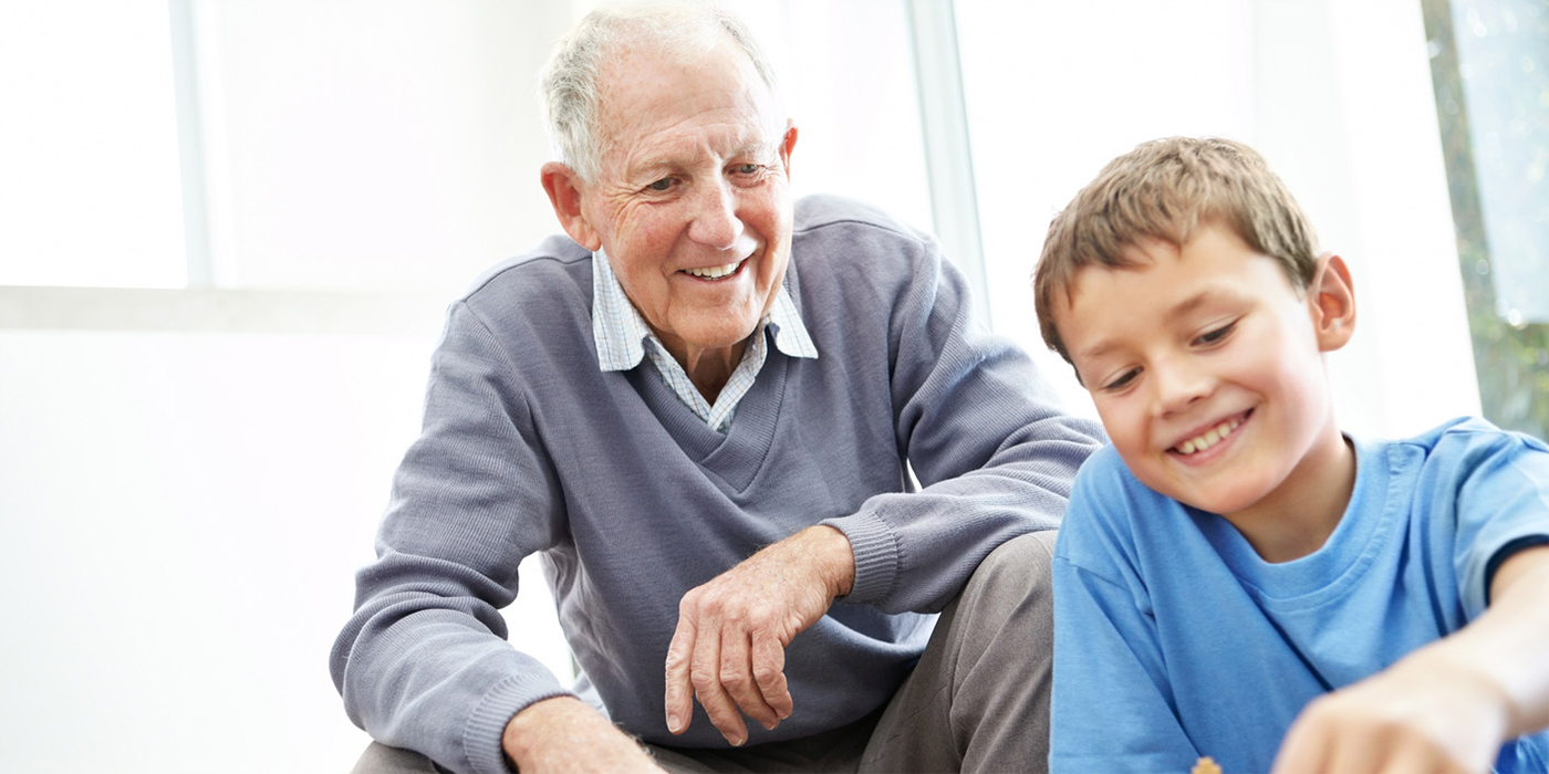 Enkelsohn und Großvater spielen gemeinsam auf dem Boden und lächeln mit gesunden Zähnen